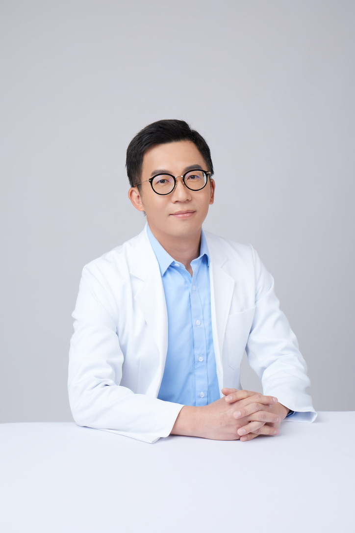 李亦倫醫師穿著白袍，雙手交握坐在桌前